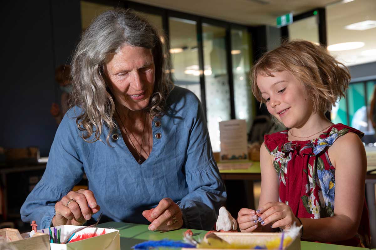 A woman and young child sit together around craft materials.