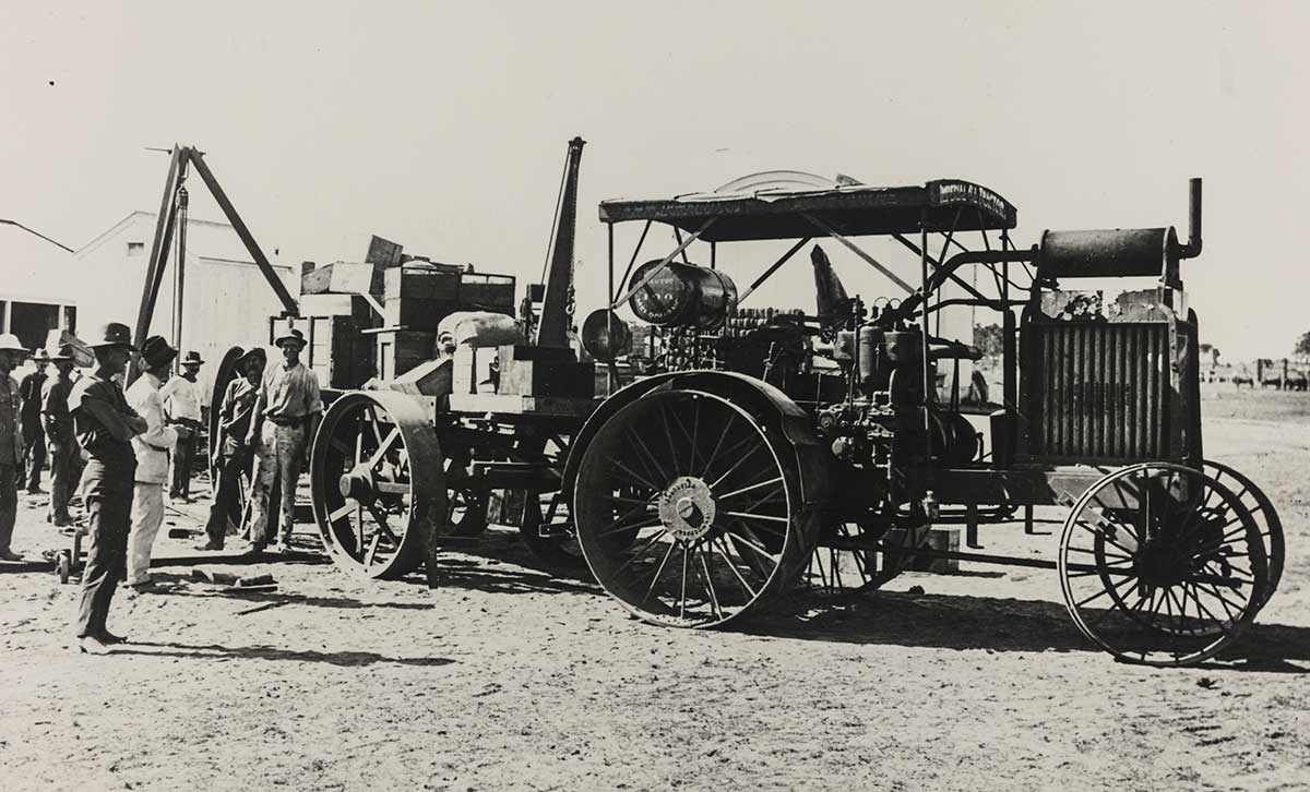 Black and white photograph of men standing adjacent to a tractor laden with crates. - click to view larger image