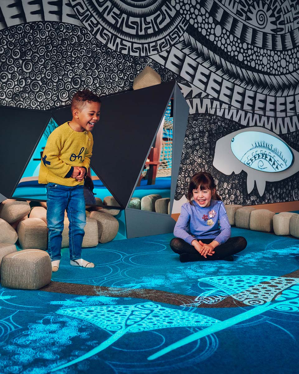 Image of two children playing in a recreational space. They are interacting with digital images of ocean scenes projected onto the floor. - click to view larger image