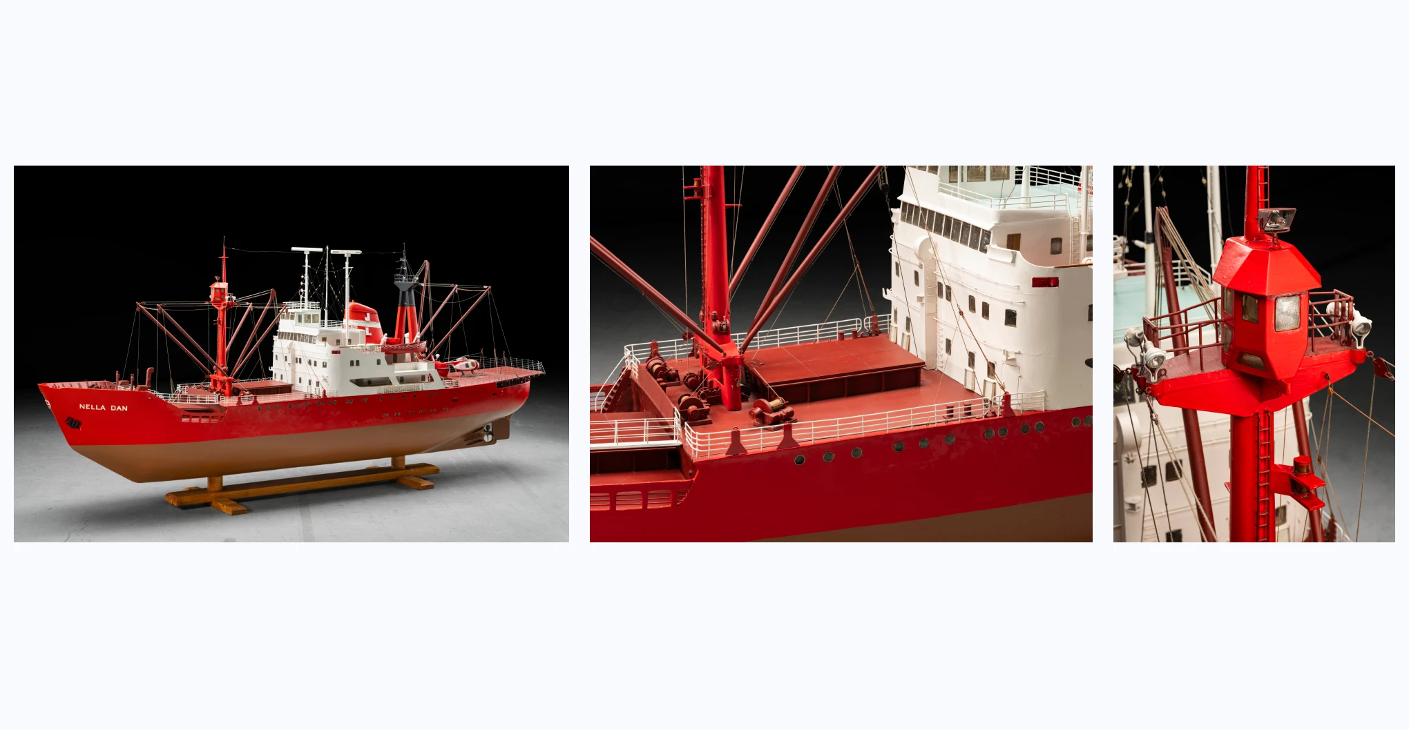 A model of a red and white ship with black trim and brown hull on a wooden stand. There is white text that reads 'NELLA DAN' painted on the stern and proper left side of the bow. The ship includes two masts with rigging, three row boats, one tug boat, brass portholes, propeller, rudder, LED lights, and an electric cable attached to one side of the hull. The model is accompanied by a red and white helicopter with black lettering below its rotor that reads 'VH-BAD'.
