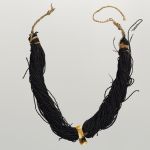 Breast ornament with hook. Hung from two black bundles of twisted human hair, connected by a cord. A pendant at the front is made of whale tooth and has the form of a hook.