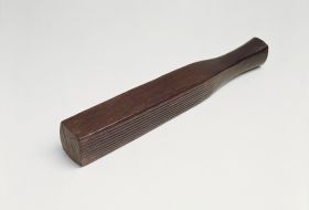 Barkcloth beater made from a piece of the heavy hardwood. Its four sides feature a number of coarser to finer grooves. The handle thickens towards the end and ends in a pyramidal shape.