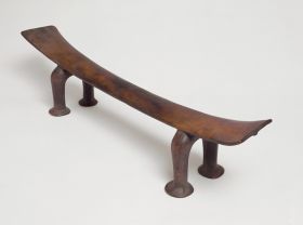 Headrest made of wood, the ‘seat’ is slightly curved and supported by a pair of horseshoe-shaped legs. The ‘seat’ becomes wider from the middle towards both ends.