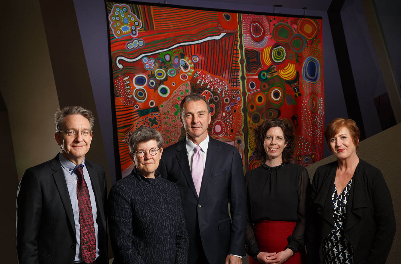 Group portrait of men and women standing in front of a painting.