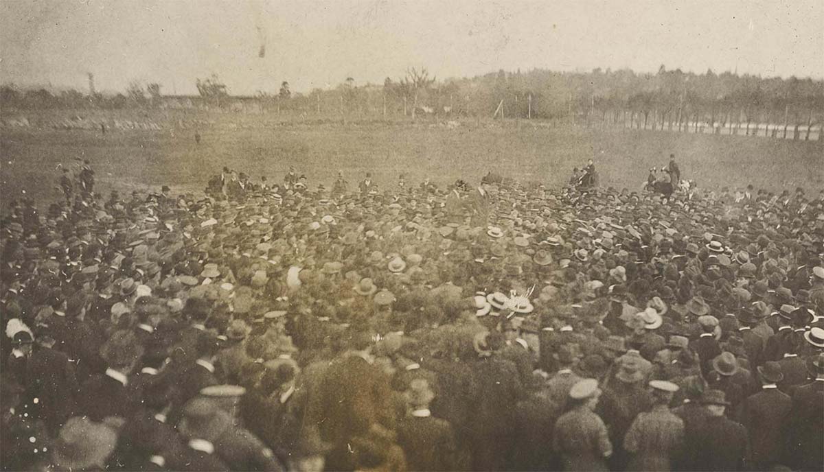 Grainy, poor-quality photo of a large crowd of men at an open expanse of grassland.
