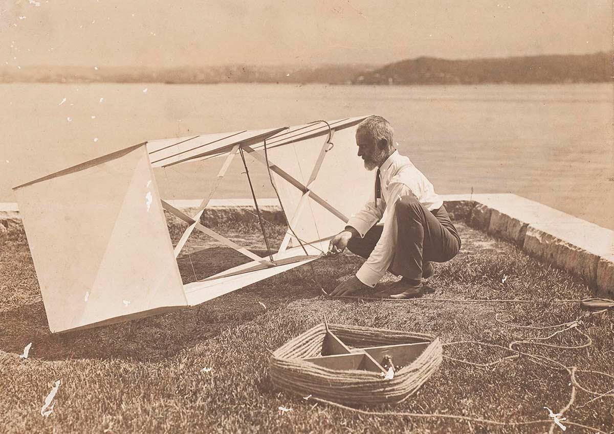 Black and white photograph of a man working on a box kite.