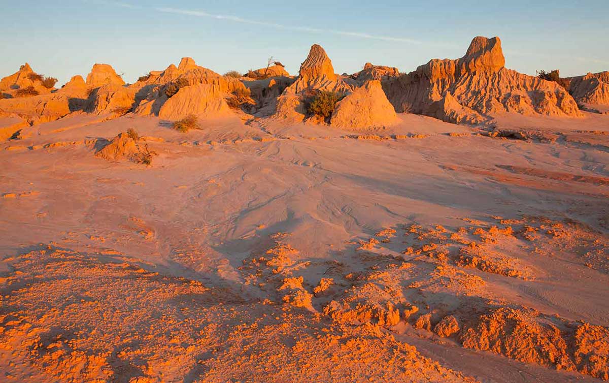 Colour photograph of ochre-coloured landscape at sunset or sunrise with a variety of outcrops.