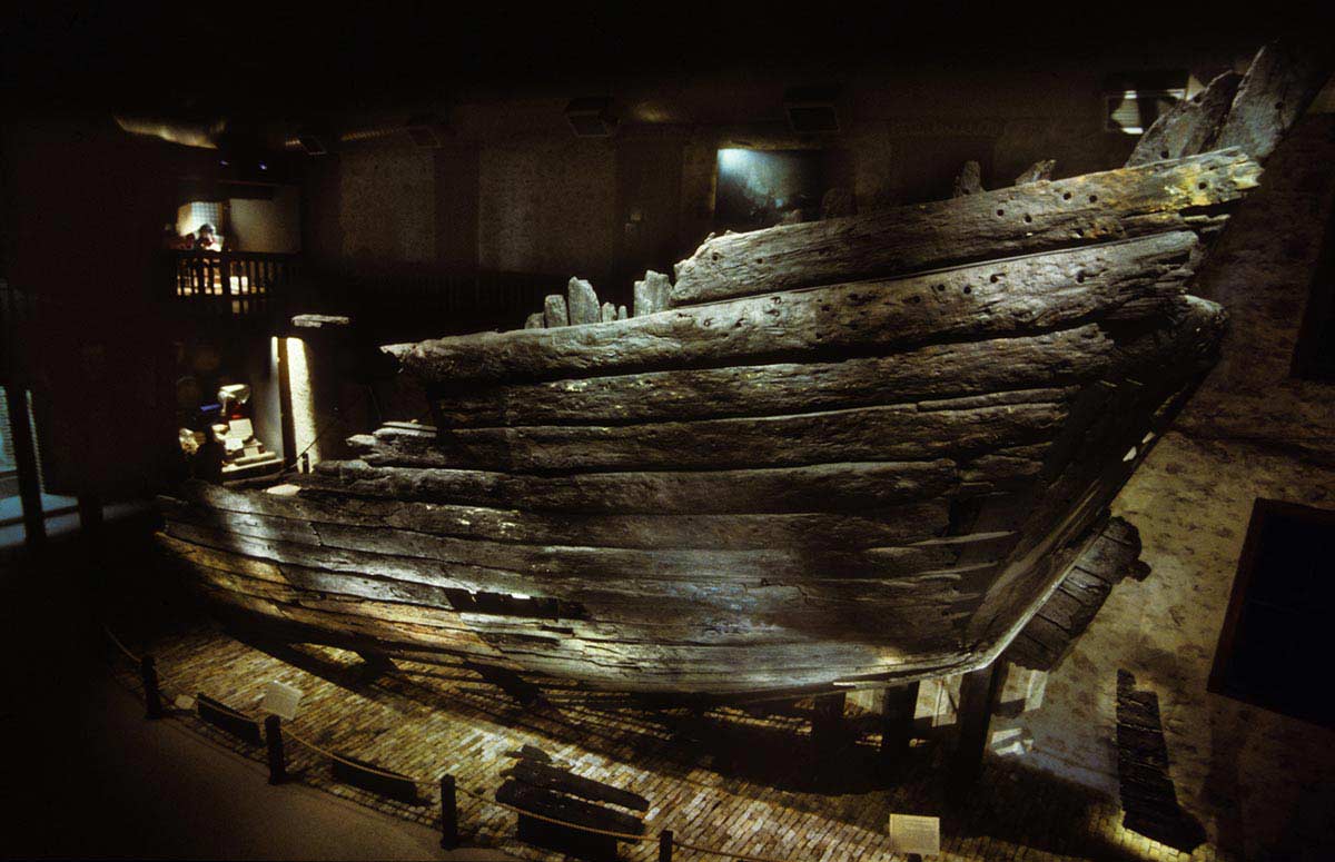 The prow or stern of a timber vessel illuminated in a two-storey exhibition hall.