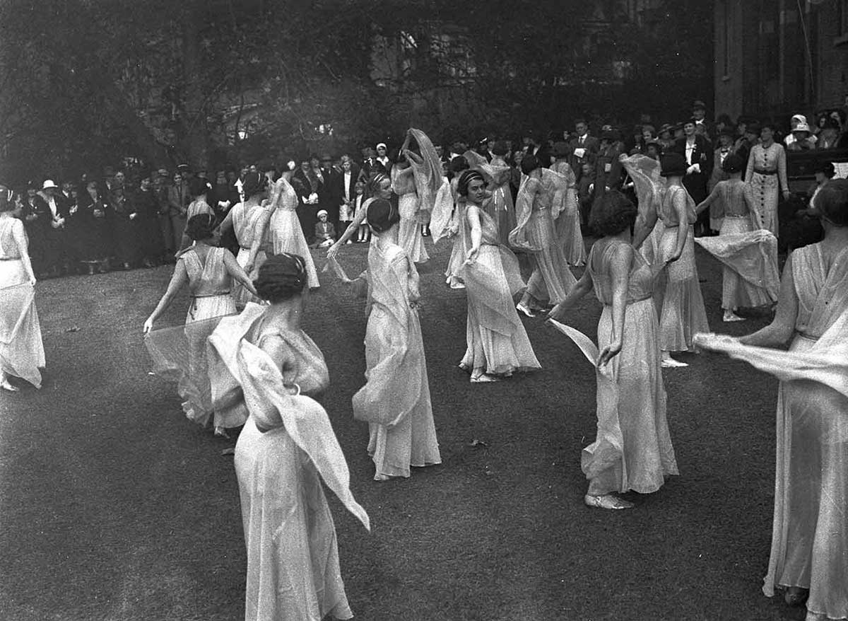 Photo taken from the rear of the stage with audience in the background. The 20 or so dancers are all wearing flowing white dresses.