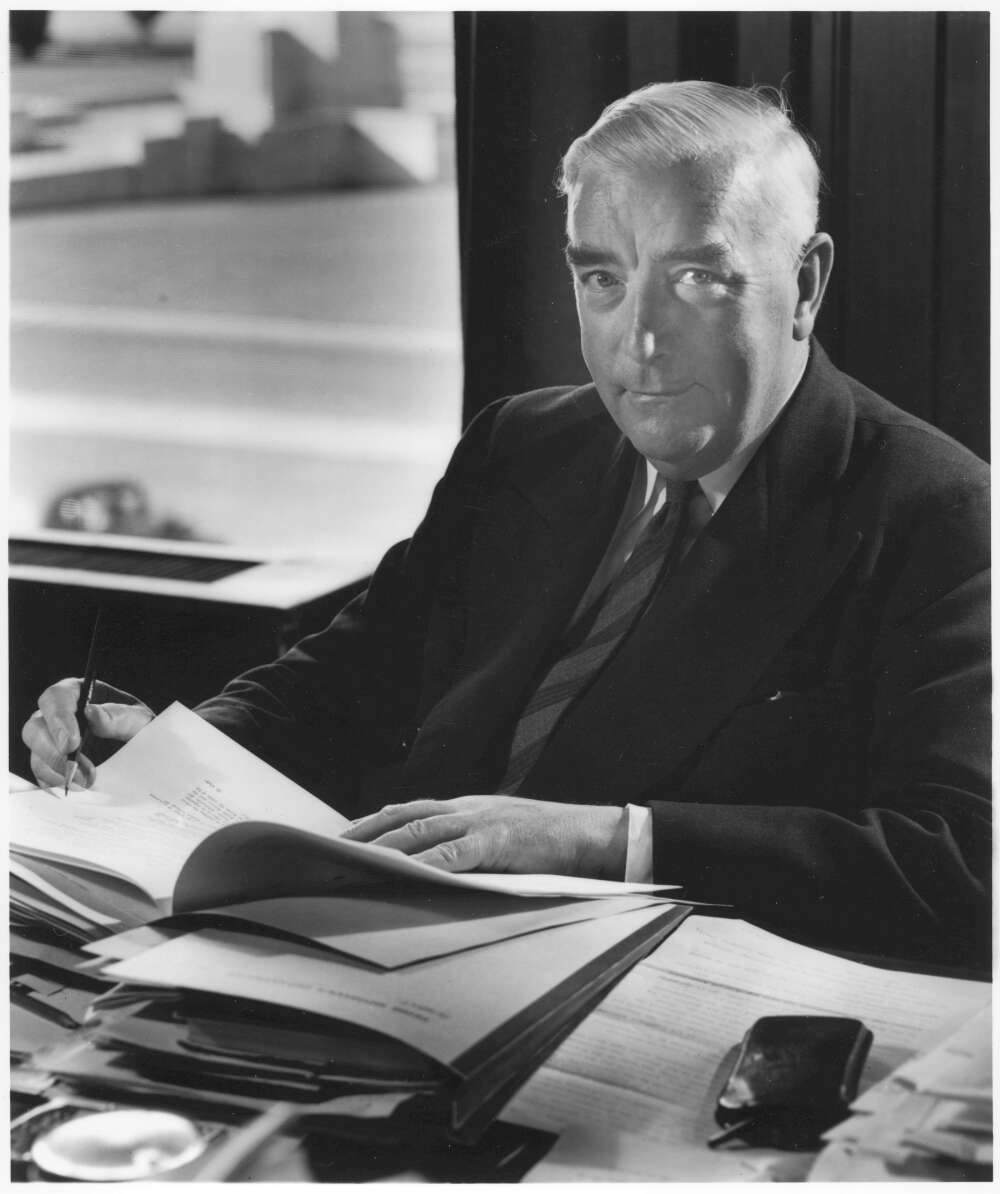Menzies at his desk in Parliament House with piles of paper in front of him. - click to view larger image