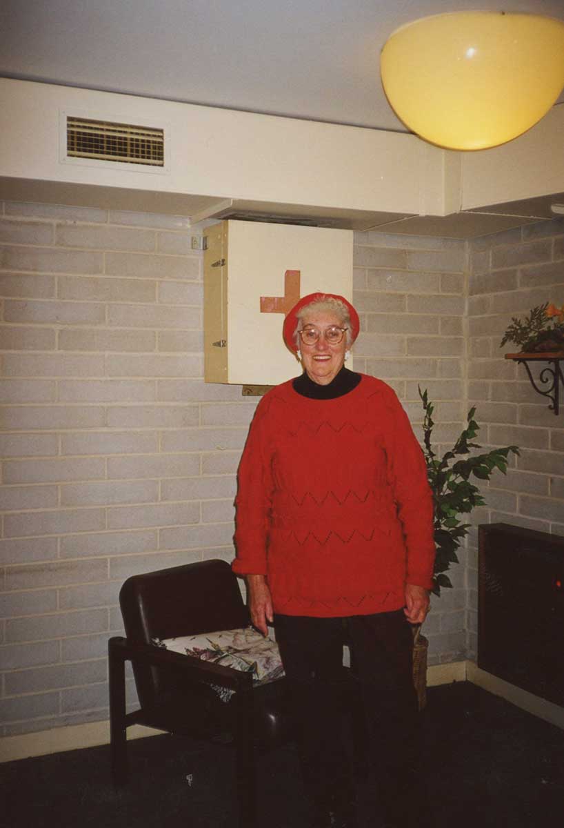 An elderly woman is wearing a red beret and jumper, while smiling for the camera. - click to view larger image