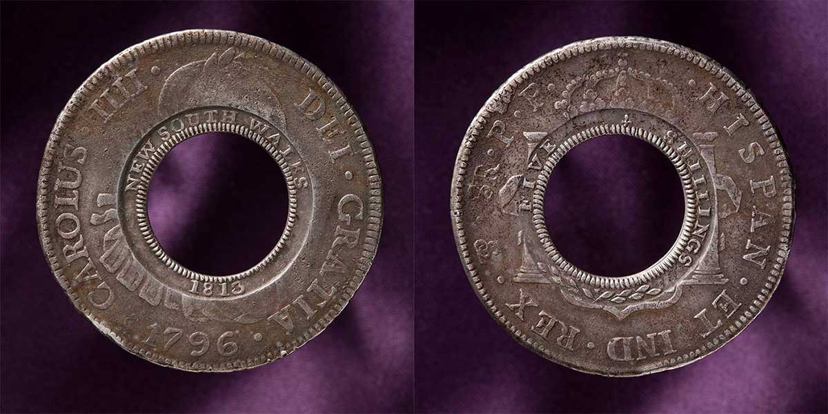 Circular coin with a hole at the centre. 'HISPAN ET IND REX' is stamped around the outer rim, with 'FIVE SHILLINGS' on the inner rim.