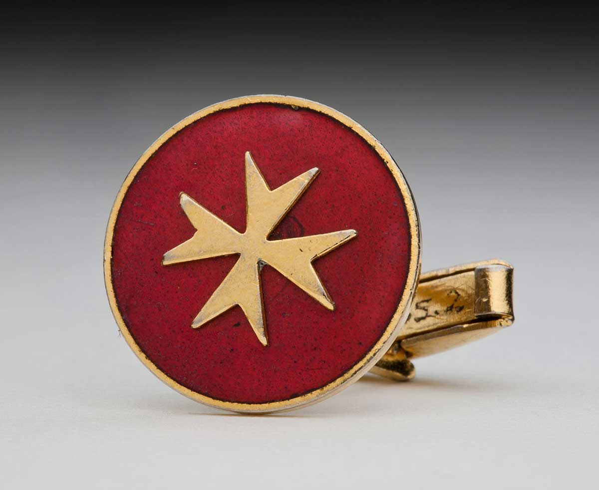 Gold cufflink with gold Maltese cross on red background. - click to view larger image
