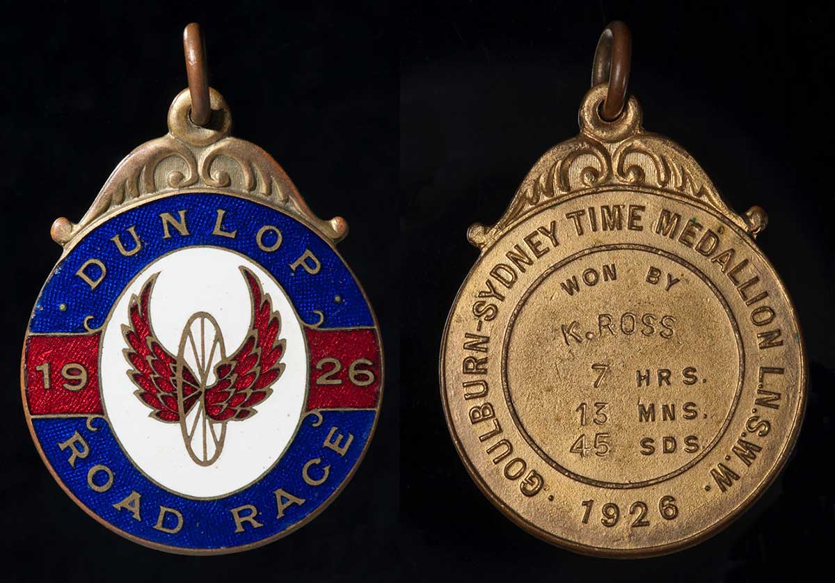 Circular metal medal with enamel in blue, red and white with text and illustration on the front and embossed and inscribed text on the back. - click to view larger image