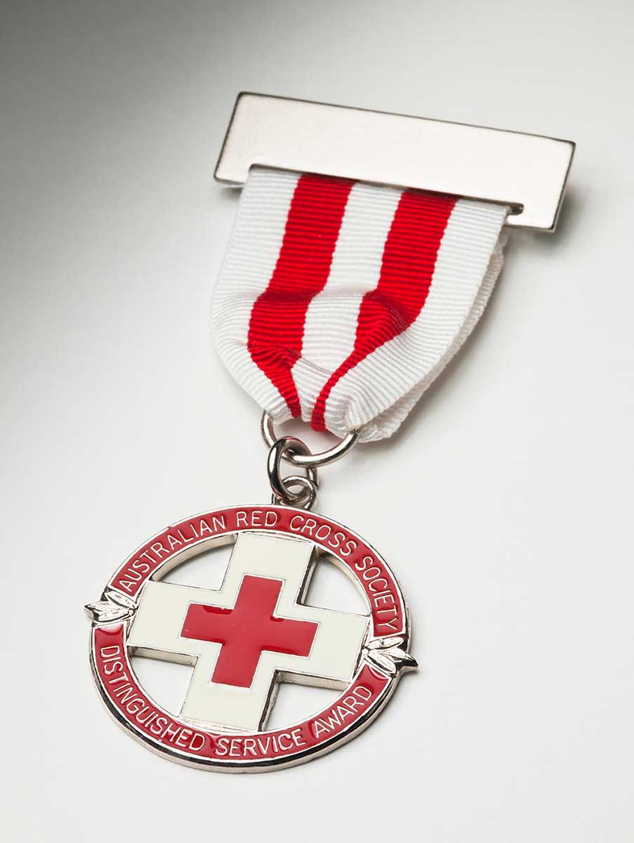 A Red Cross badge hanging from a silver bar and a ribbon with vertical white and red stripes. The circular award features a central red on cross on silver background, with the words 'AUSTRALIAN RED CROSS SOCIETY / DISTINGUISHED SERVICE AWARD' on an outer circle. - click to view larger image