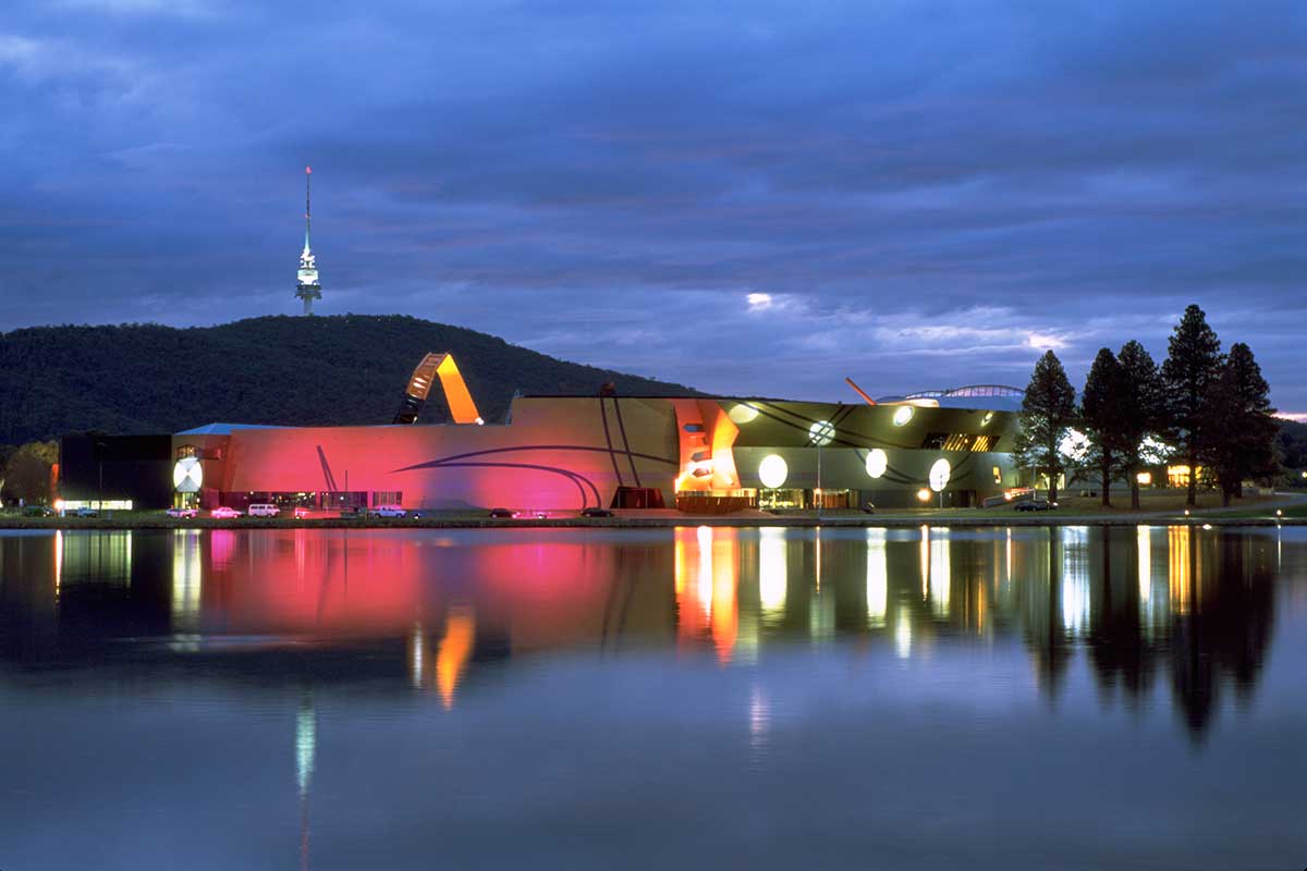 Panorama of a modern building at dusk overlooking a lake. 