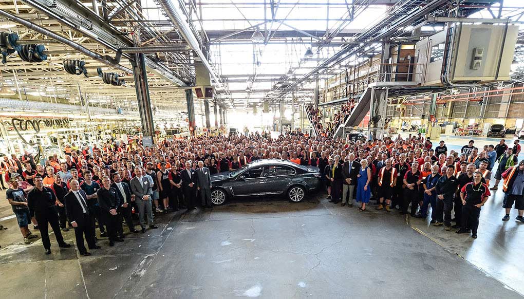 A crowd of people gather around a car and pose for a photograph.