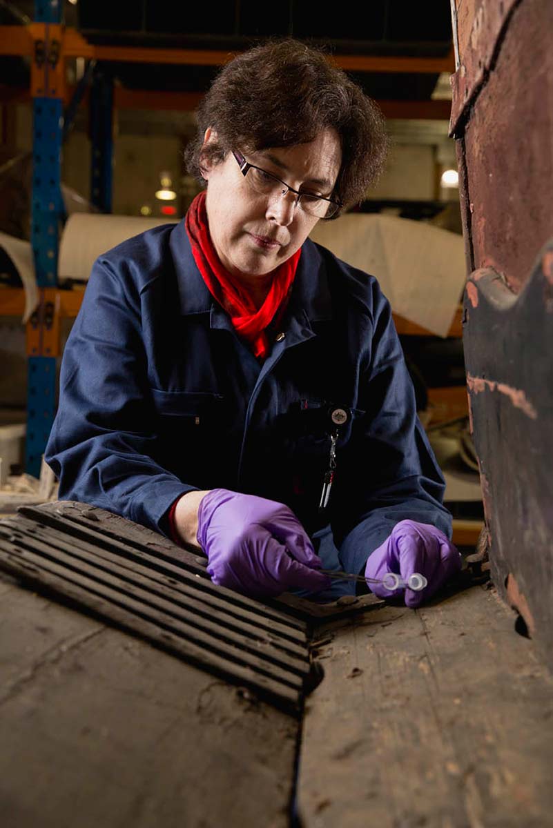 A female conservator wearing gloves is working on a large antique object. - click to view larger image