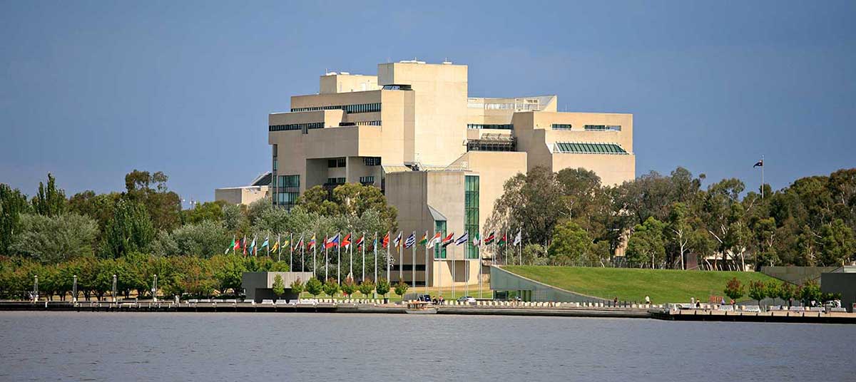 Colour photograph showing an exterior view of the High Court, taken from across the lake. A row of flags flies on the lake shore, outside the court building. - click to view larger image