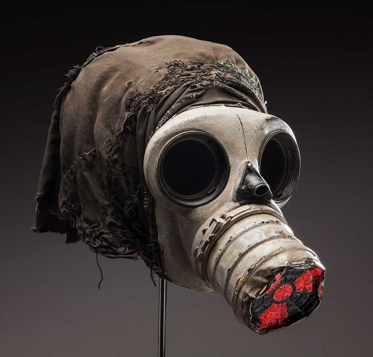 Gas mask with black cloth attached to the back and the international symbol for radiation painted in red on the nose cone.