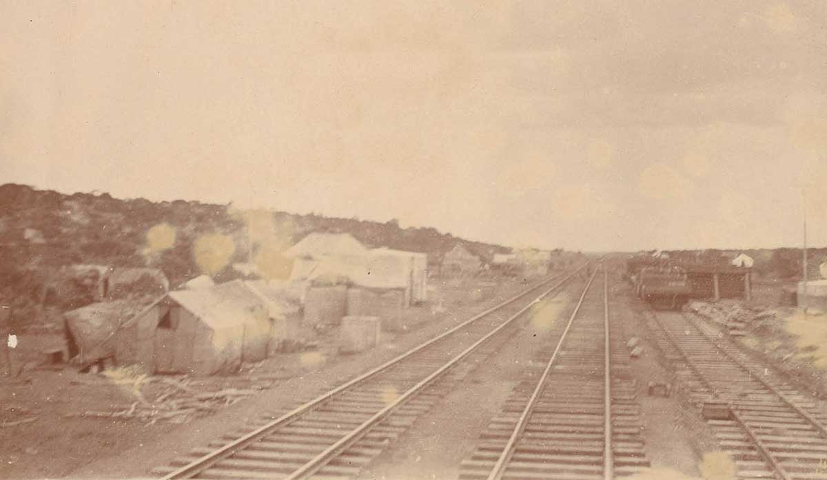 Deteriorated sepia photo showing three tracks with a cluster of tents to the left. - click to view larger image