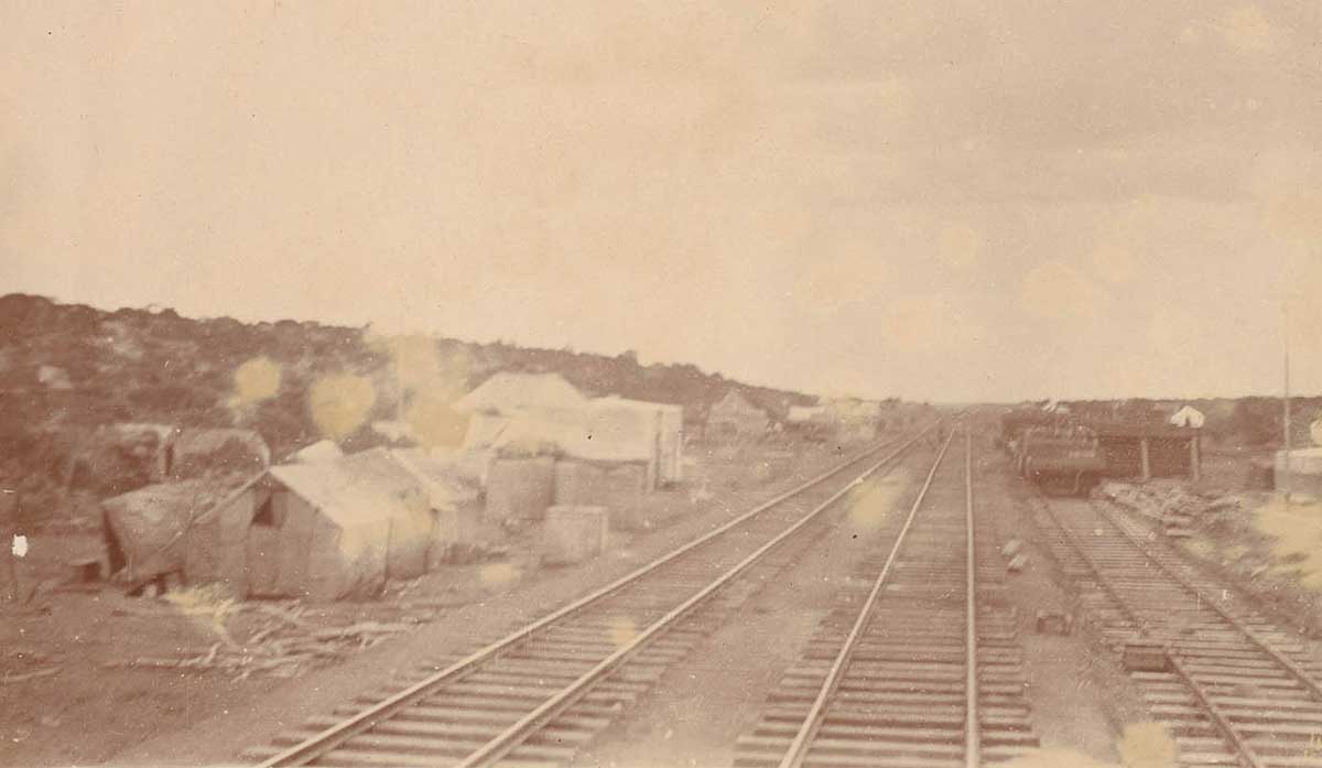 Deteriorated sepia photo showing three tracks with a cluster of tents to the left - click to view larger image