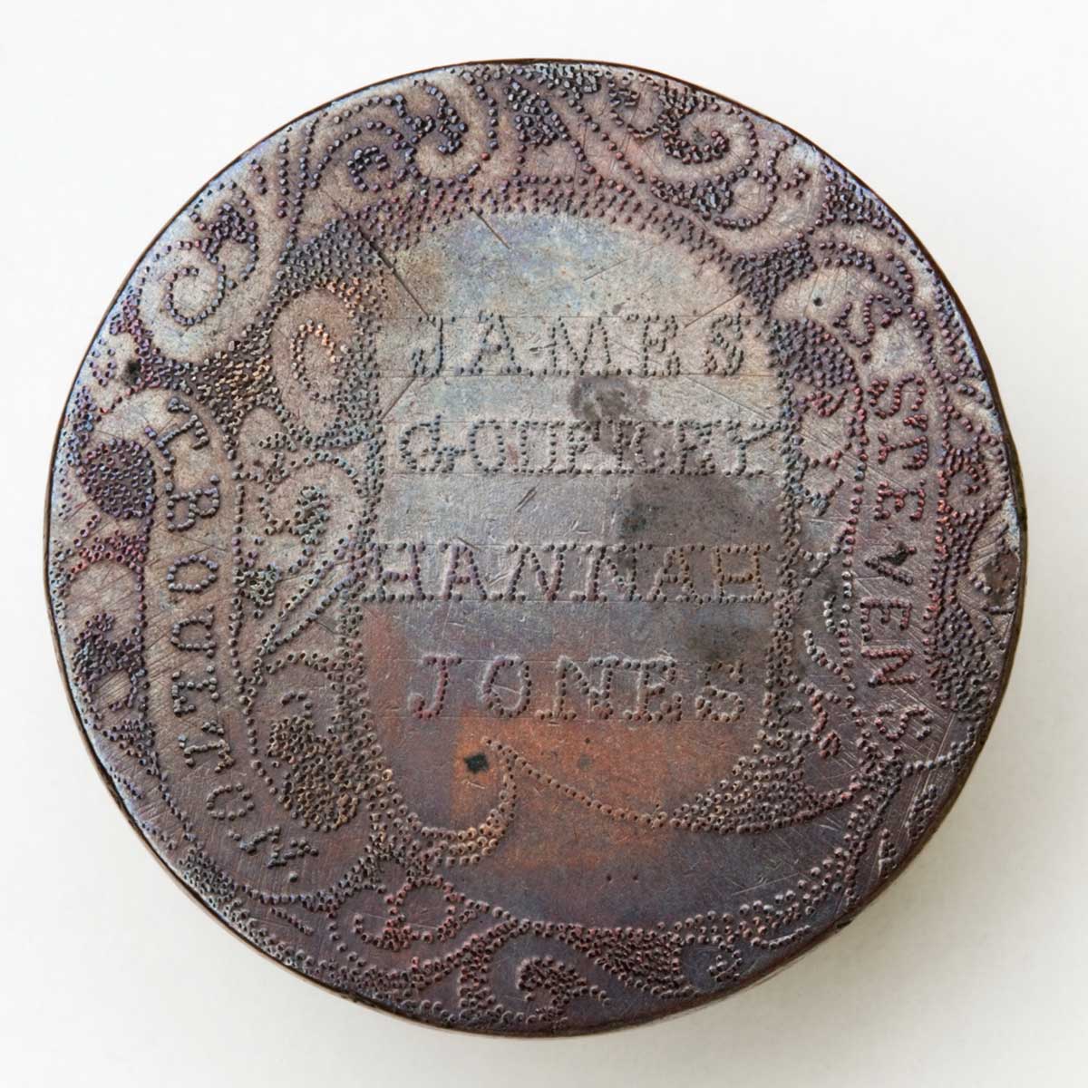 Token engraved with an elaborate swirling stippled design and a scroll shape containing stippled text. To the left and right of the main text are the names: T. BOULTON. S. STEVENS. Within the scroll are the names: JAMES GODFREY HANNAH JONES. - click to view larger image
