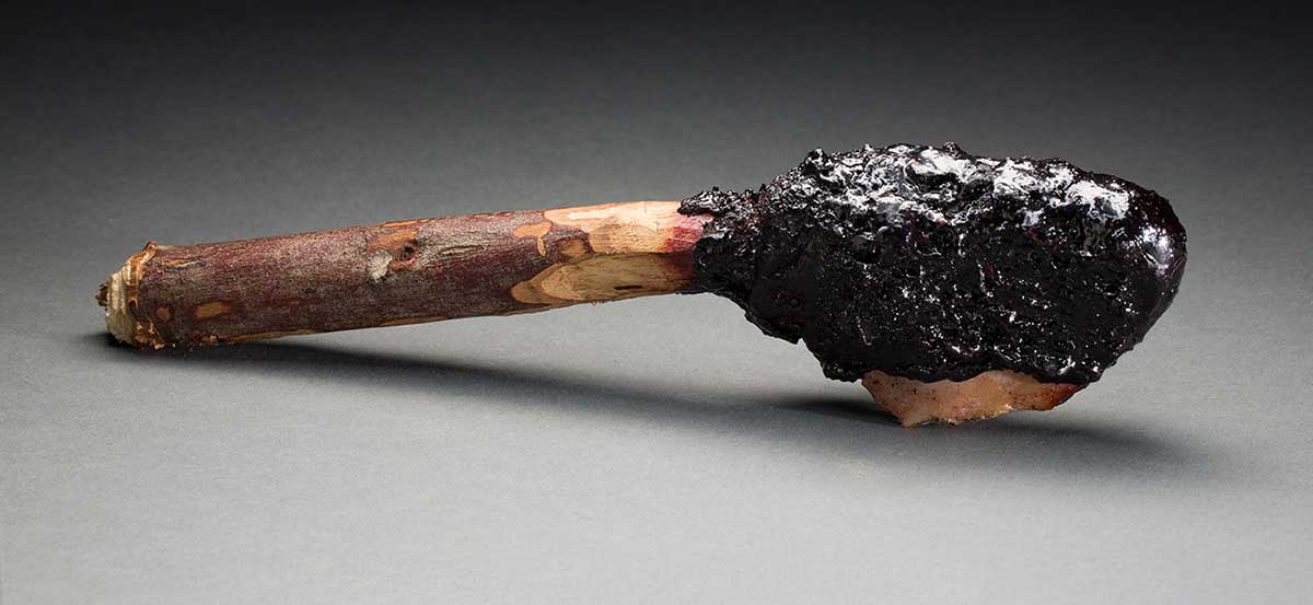 A stone axe made of a wooden stick attached to a stone and resin at the top end of it.  - click to view larger image