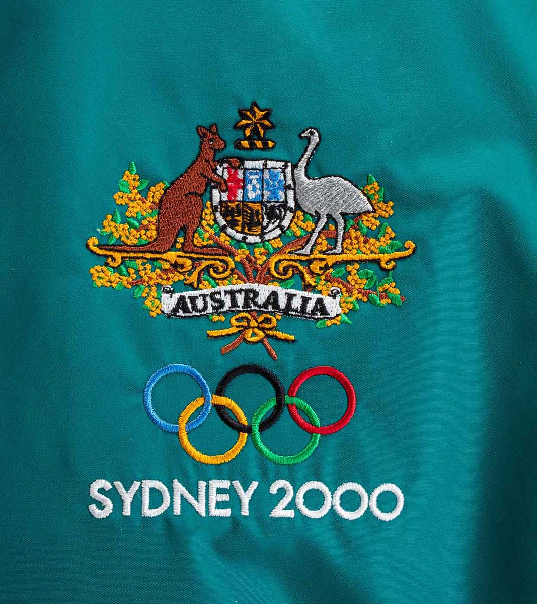 Close up of a tracksuit top with the Australian coat of arms and 'Sydney 2000' embroidered on it. - click to view larger image