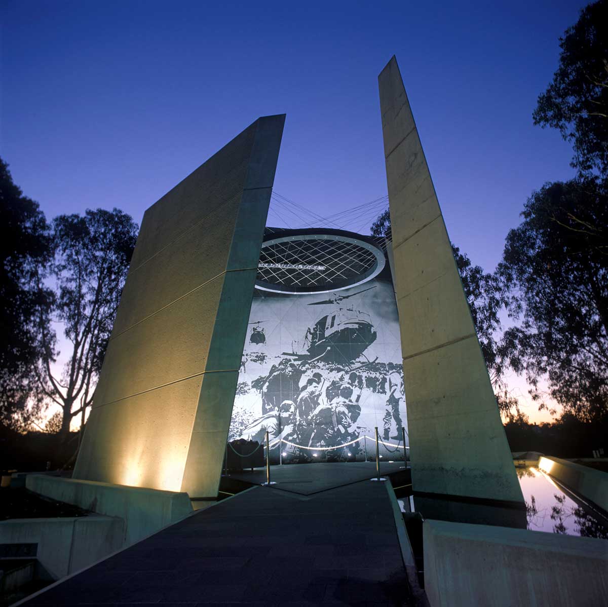 photo taken at dusk showing the illuminated memorial depicting the photo above of the soldiers waiting for a helicopter to land - click to view larger image