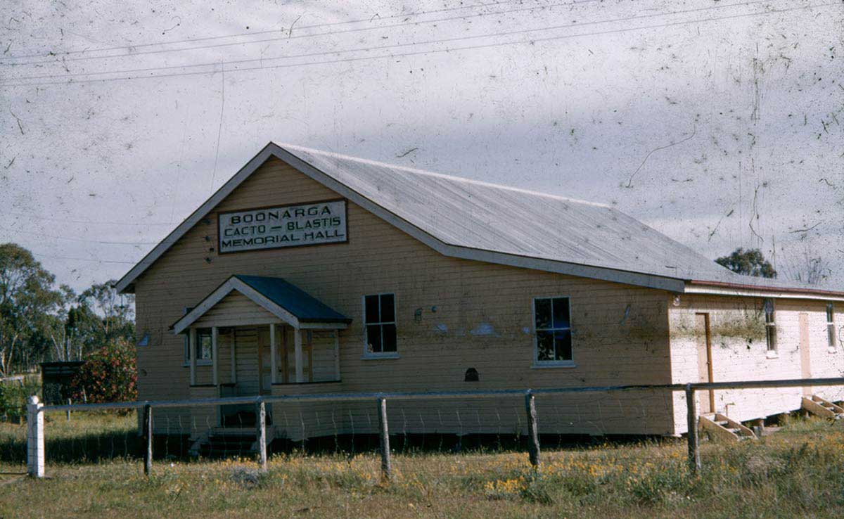 A single-storey weatherboard building, painted pale yellow, with a corrugated iron roof. A painted sign above the front entry says: 'Boonargo Cacto-Blastis Memorial Hall'. - click to view larger image