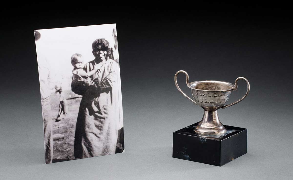 Black and white photograph of a woman holding a baby; and a small mounted silver cup. - click to view larger image