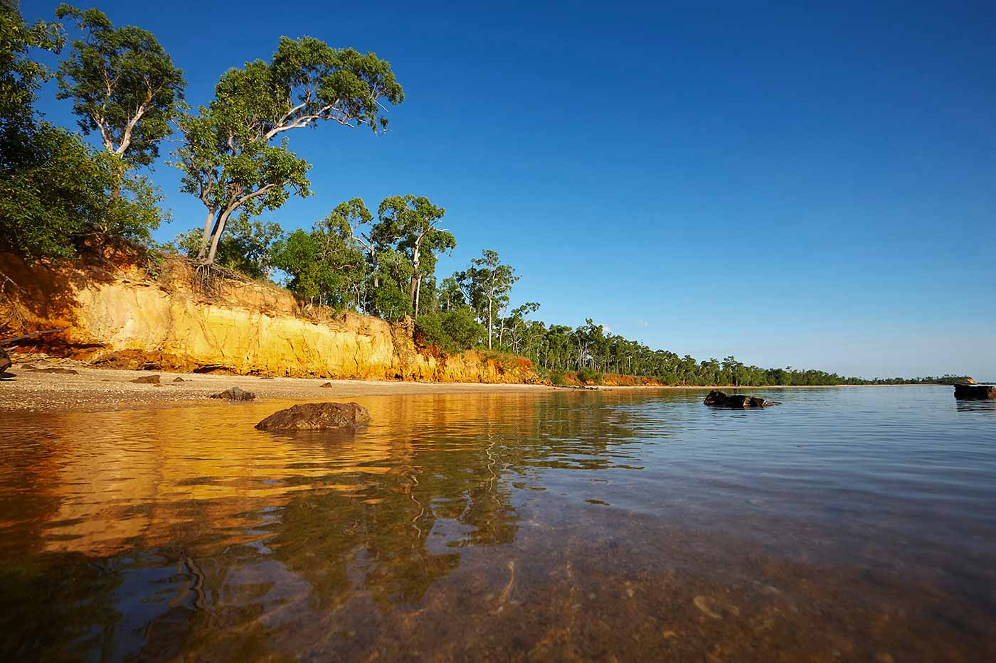 View of yellow ochre sheer rock formations and trees running alongside a river with clear and calm waters.