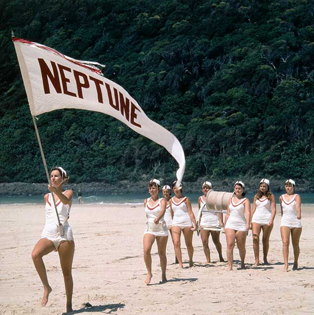 Members of the Neptune Ladies' Lifesaving Club marching on the beach, Tallebudgera, Queensland, 1957. The leader is carrying the Neptune club flag. - click to view larger image