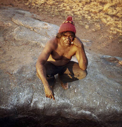 Portrait photo of an Aboriginal Australian man crouched down wearing a beanie. - click to view larger image