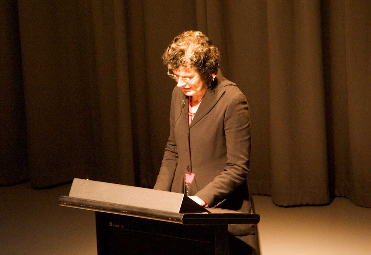 A woman stands at a lectern on a stage. - click to view larger image