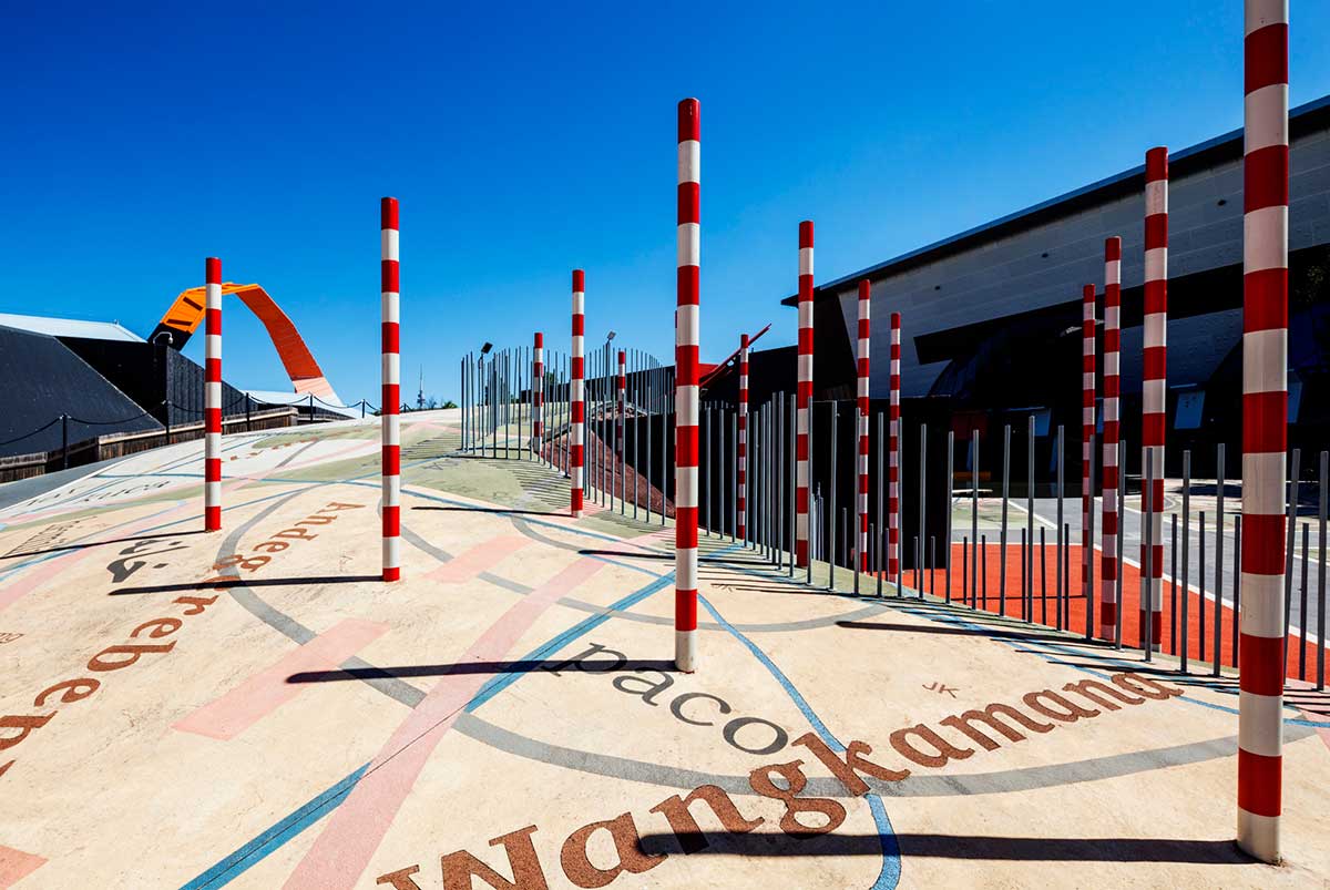 An outdoor museum space highlighting various sculptural features including a series of red and white striped poles. 
