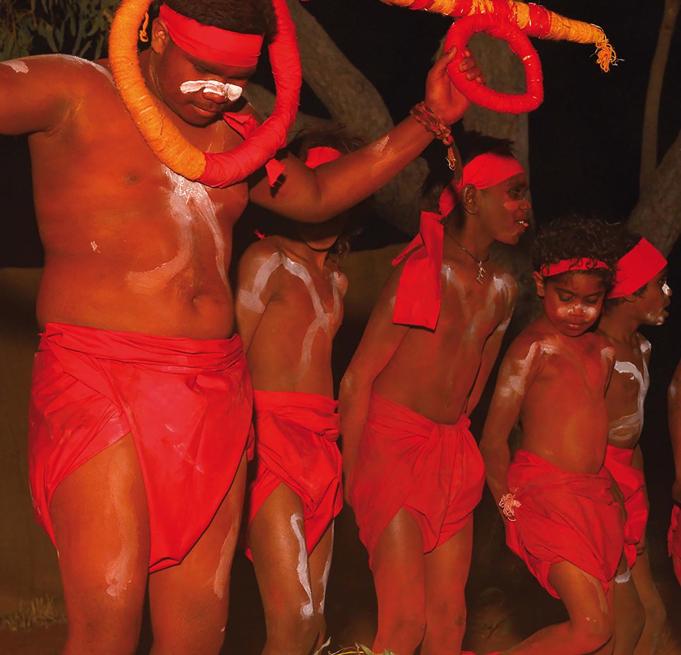 Colour photo of a group of young male dancers performing in red attire.