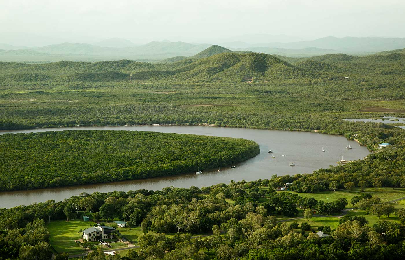 Aerial photograph of a river winding its way through lush green countryside. Several boats are moored on the river.