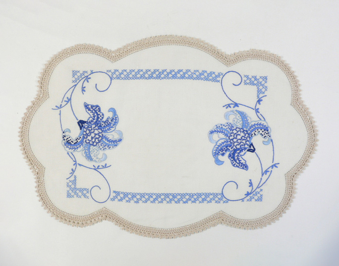 A hand-embroidered doily with a crocheted border. The embroidery is on linen in several shades of blue and features a cross stitch 'frame' with a tiger lily motif at either end. - click to view larger image