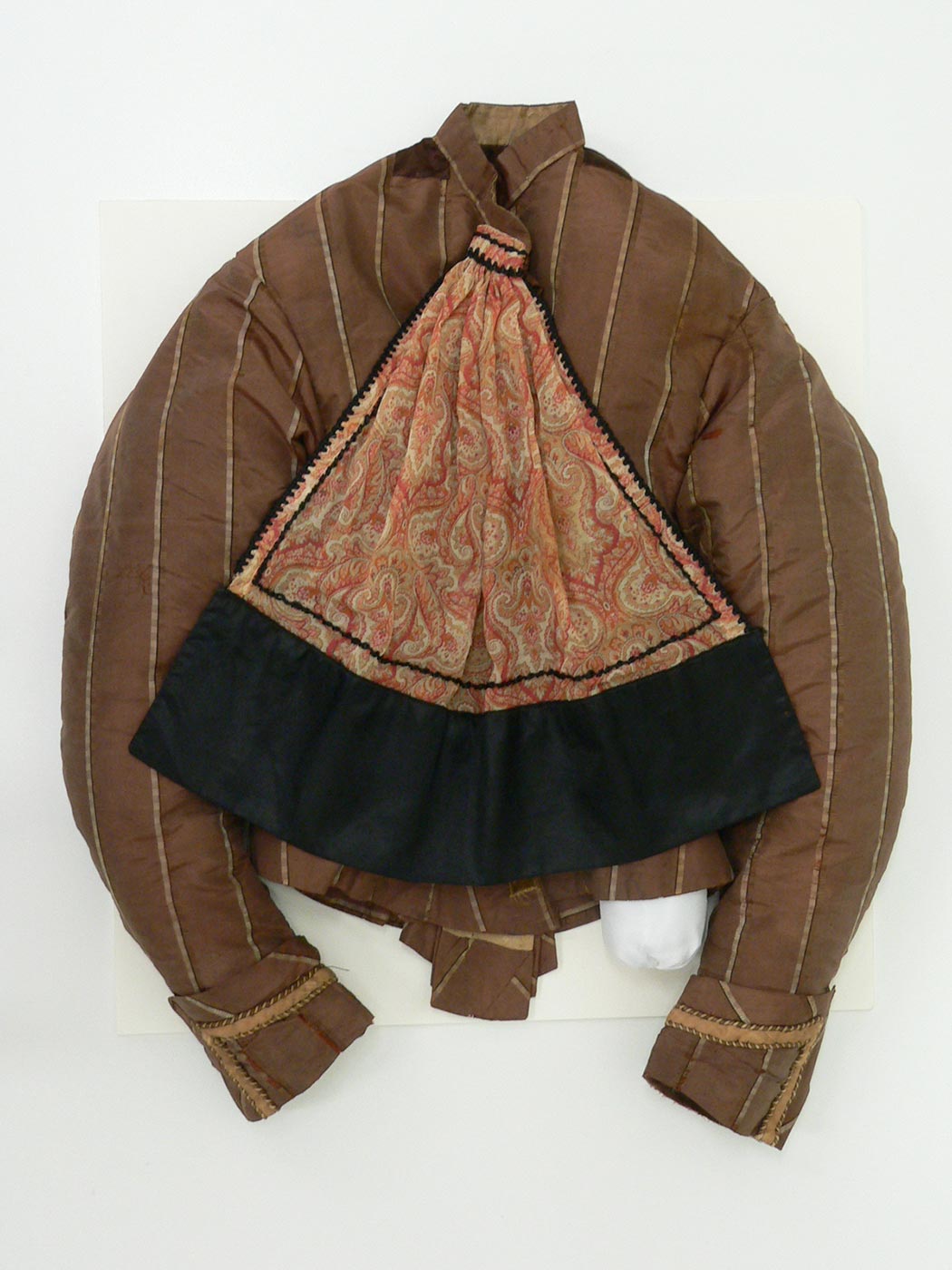 Colour photograph of a brown coloured jacket with vertical cream stripes and cuff trim. A paisley scarf with black trim is attached at the collar. - click to view larger image
