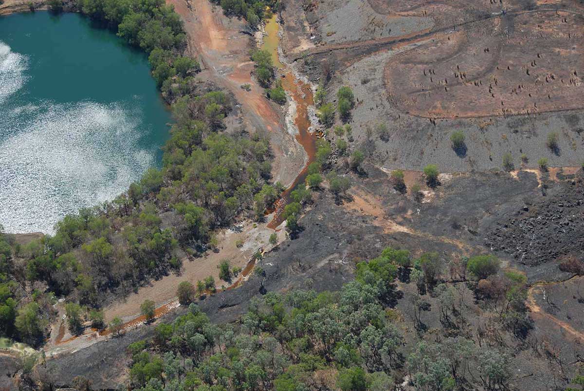 Colour photo of an aerial view of an open pit mine next to a lake.
