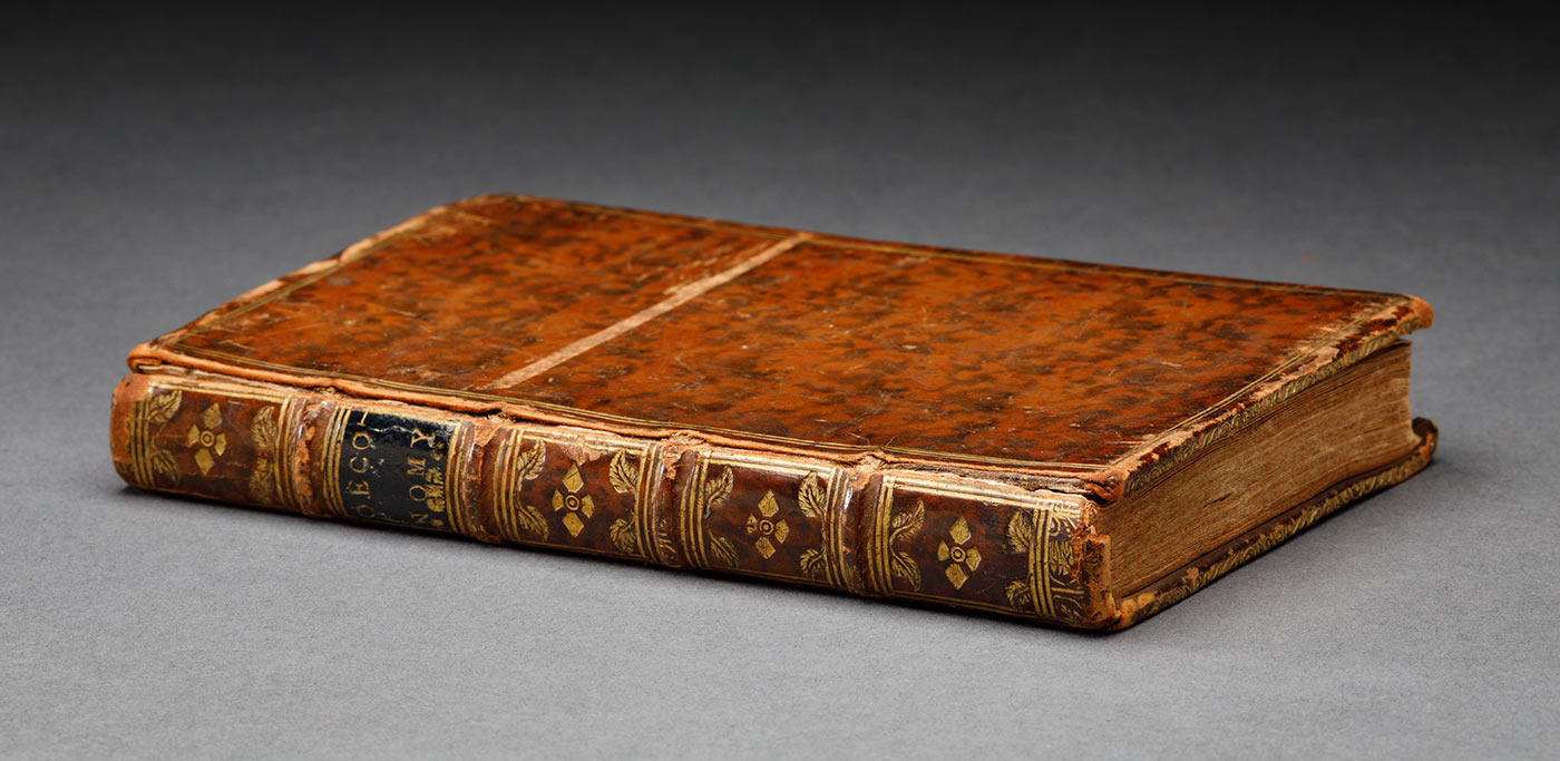 A book featuring the title 'The Oeconomy of Human Life' on the title page. It has a brown mottled leather cover with a gold border. The front hinge is cracked and the top of the front cover is scuffed. The title-page has the text [handwritten by William Perry] in black ink that reads 'This book went round the World on the Endeavour in 1768 / 69 / 70 & 1771', with Perry's signature underneath. - click to view larger image