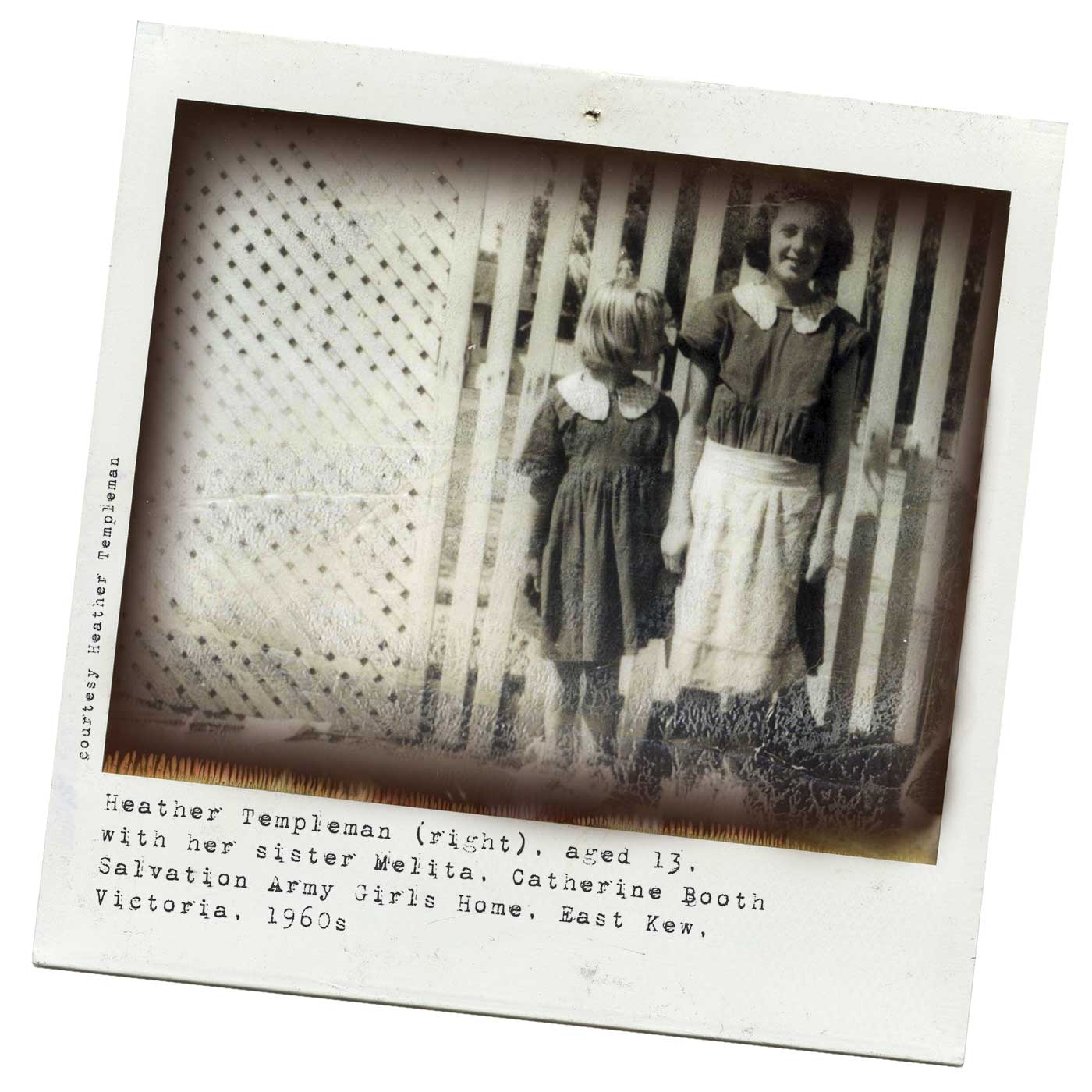 Polaroid photograph showing two girls standing in front of a white lattice fence. The smaller girl, on the left, turns her head to look at the older girl. Tyepwritten text below reads 'Heather Templeman (right), aged 13, with her sister Melita, Catherine Booth Salvation Army Girls Home, East Kew, Victoria, 1960s'. 'Courtesy Heather Templeman' is typed along the left side. - click to view larger image