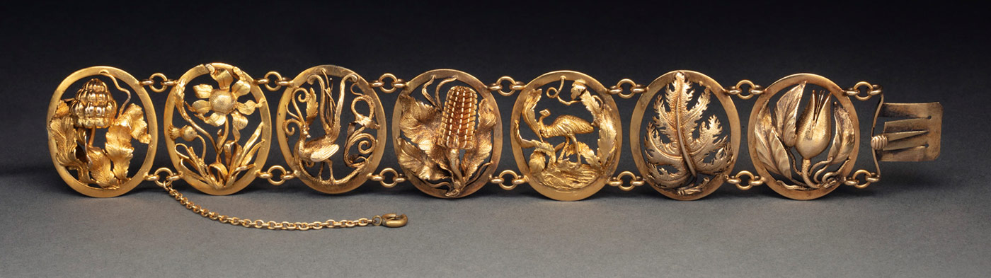 A finely rendered gold openwork bracelet comprising seven linked panels. Each panel depicts an Australian motif including a waratah, a flannel flower, a lyrebird, a banksia, an emu, a fern and a native pear. It also has a safety chain attached to one end.