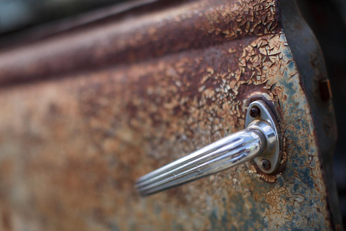 Detail of a silver handle attached to an old rusty car door. - click to view larger image