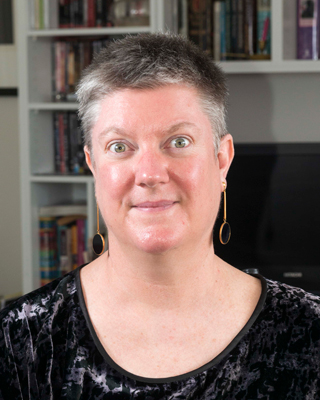 Photograph of Christina Ryan. Christina has short grey and black hair and is smiling. 