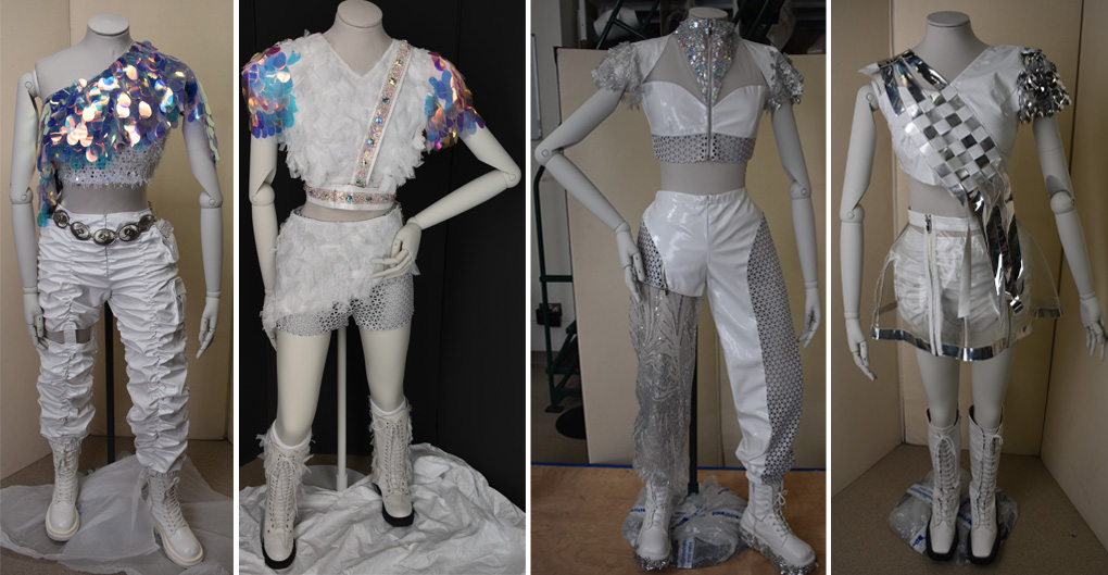 Four futuristic costumes worn by Aespa. The colour scheme is white and silverwith irridescent accents; the waists are high, revealing midriffs with cropped tops.   The costumes from left to right were worn by the different actors of the band, Giselle, Ningning, Winer, Karina.