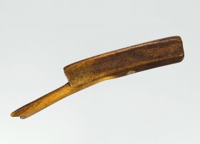 Bark beater made of a piece of whalebone, the head is trapeze-shaped and the end of the flat grip is wide and notched like a fishtail.