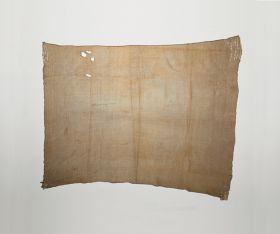 Hand-woven cloak of brown-beige colour made of flax, with remnants of dog fur strips on all four corners.